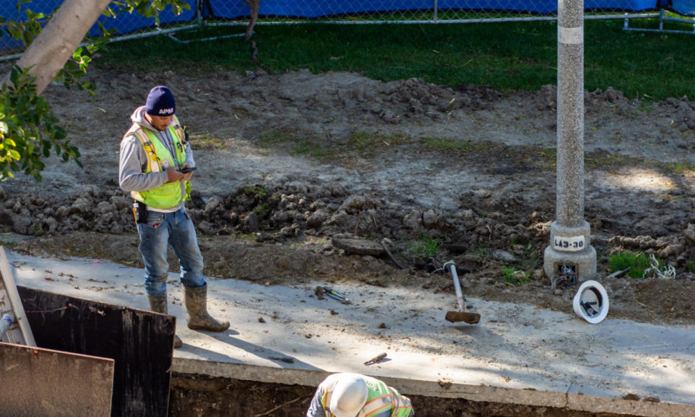 Photo contains: two construction workers working in a trench in the dirt to fix water pipes.