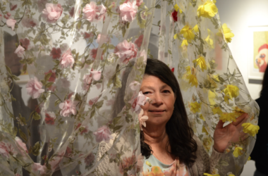 Picture Contains: A woman walking through a translucent fabric art pice that is covered in pink and yellow cloth flowers.