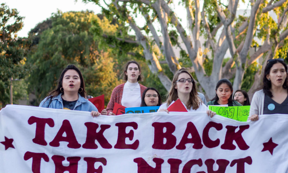 Students hold a large white sign that has "take back the night" written in red.