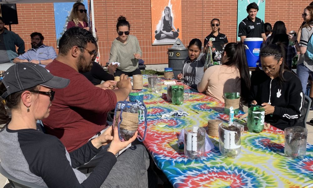 People sit crafting around a table with a tie-dyed cloth on top.