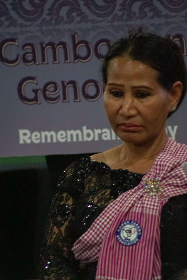 Woman stands in front of Cambodian Genocide Remembrance Day sign.