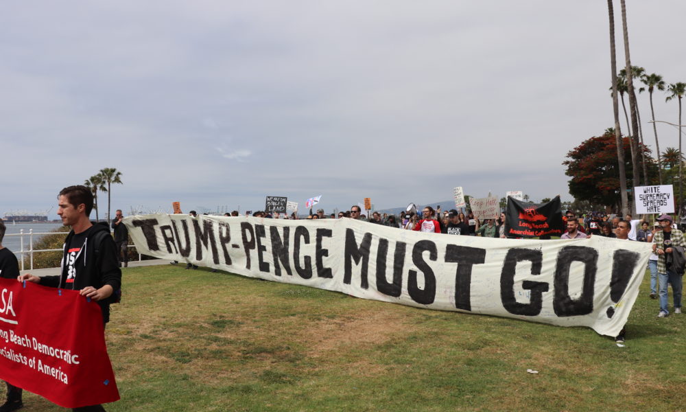 Protestors hold banner that says "Trump Pence Must Go."
