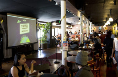 Students sit in The Nugget in front of a screen that says "Trivia Tournament for Earthlings"