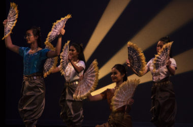 four women hold ornate hand fans and wear traditional Cambodian clothing.
