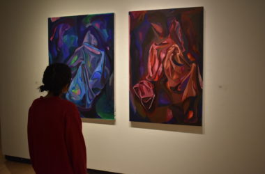 a young woman looks at two vertical paintings one blue one red.