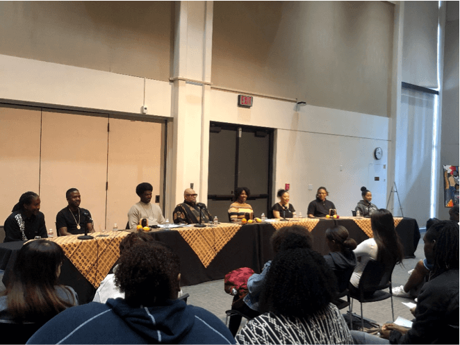 A panel of African American people speak to a packed auditorium