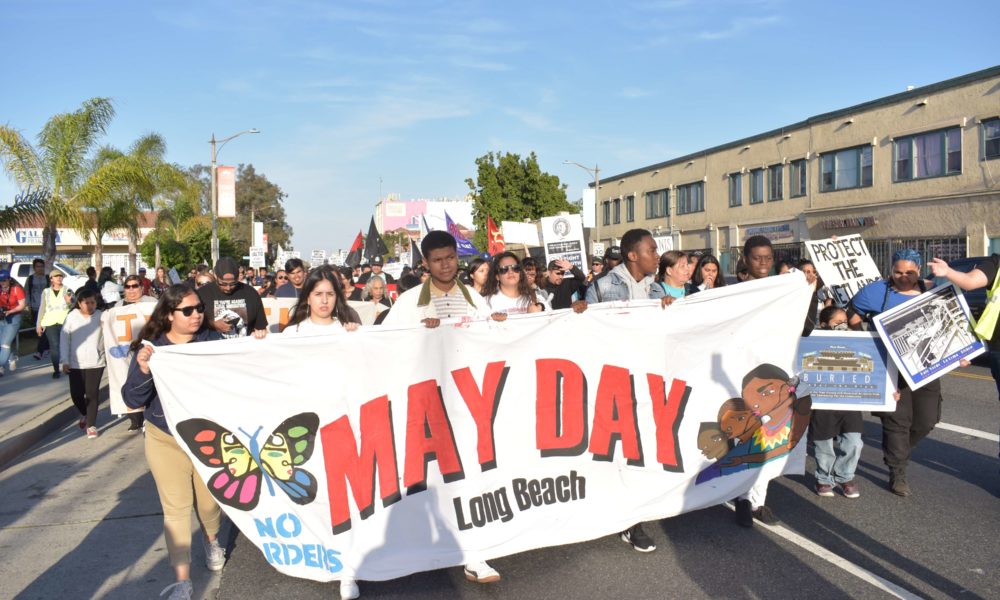 Marchers from Long Beach walk down street with "May Day" banner