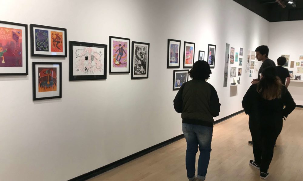 Students view various works of illustrated art on a white wall