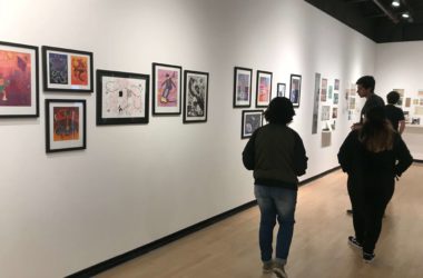 Students view various works of illustrated art on a white wall