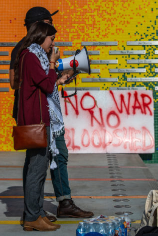 A woman holding a megaphone stands in front of a man and a sign that reads "No war no bloodshed."