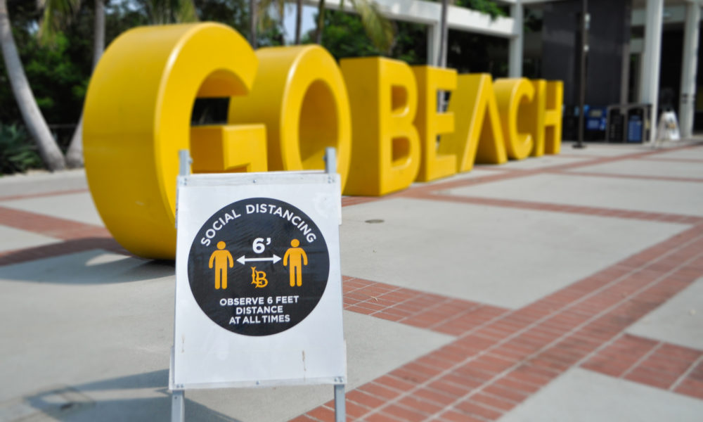 A sign cautioning people to stay six feet away from one another sits in front of the GO BEACH sign