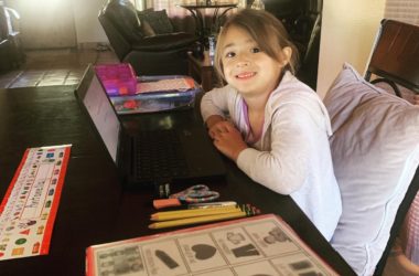A little girl sitting at the kitchen table with her homework and laptop