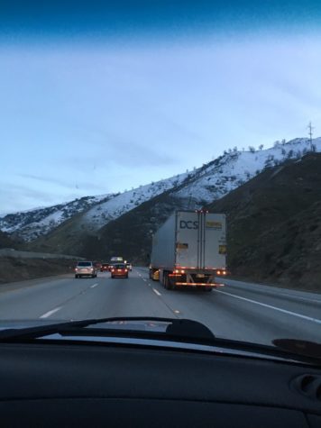 Cars and trucks drive along a freeway with snow covered mountains in the background