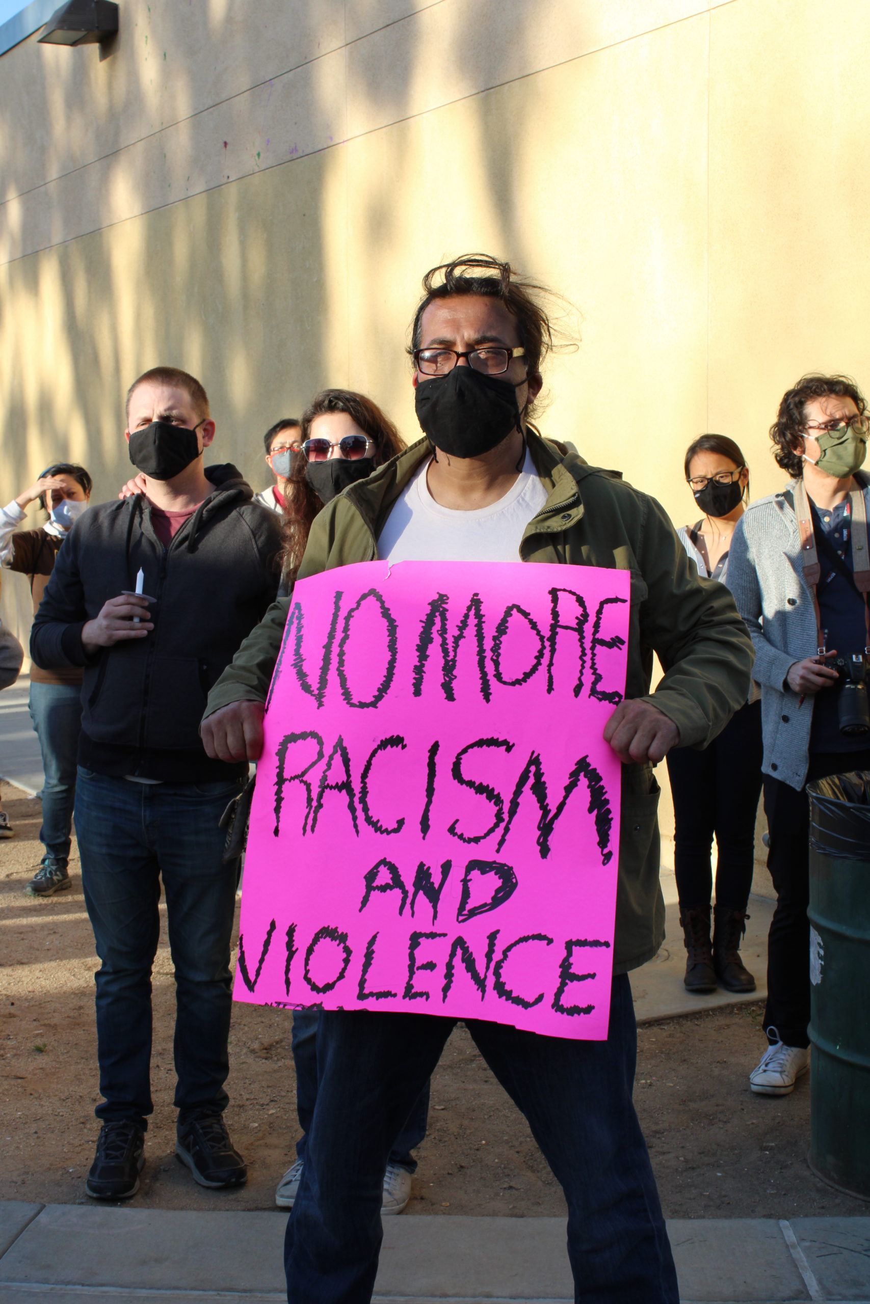 A man holds a pink sign that reads "No more racism and violence."