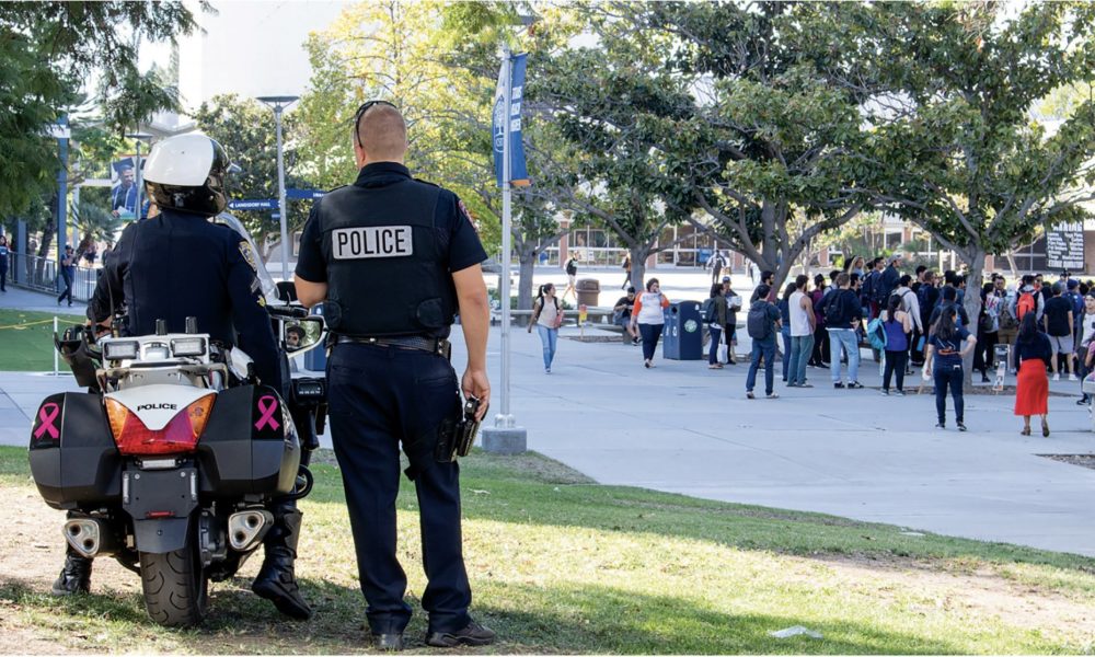 Two police officers watch a crowd on a college campus one sits on a motorcycle