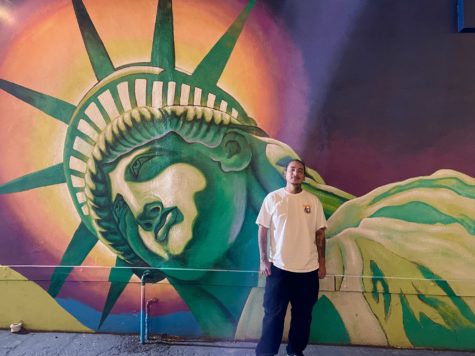 Bixby Knolls Tattoo shop owner, Sergio Parga standing by mural outside of his business (He/Him)