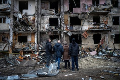 Photo depicting four Ukrainian citizens looking at an apartment building that has been damaged by a Russian rocket in Kyiv on Feb. 25.