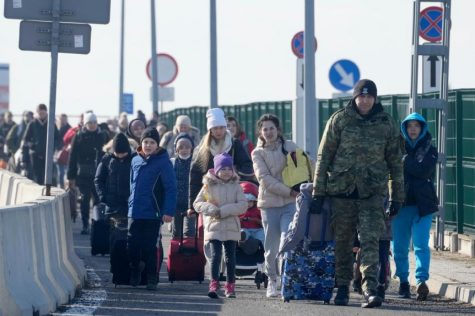 Photograph showing a Polish border agent helping Ukrainian refugees cross into Poland on foot.