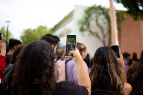 Three students standing in the crowd hold up their phones to record and take photos of Sister Cindy's sermon.