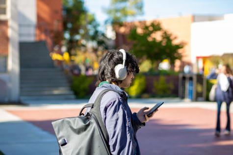 A students wears headphones while walking toward the Hall of Science.