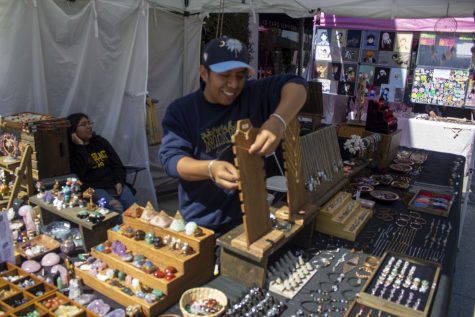 Jose Fernando Melquiades restocks necklaces at his jewelry vendor in the campus flea market outside the bookstore.