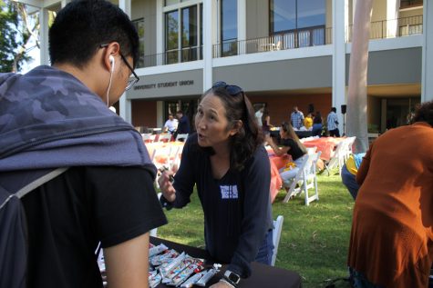 Diane Hayashino with Counseling and Psychological Services (CAPS) speaks with students during Cultural Welcome Week. Hayashino looks to be giving out some food during the evening hours of the Asian/Asian American Welcome event at the USU North Lawn.
