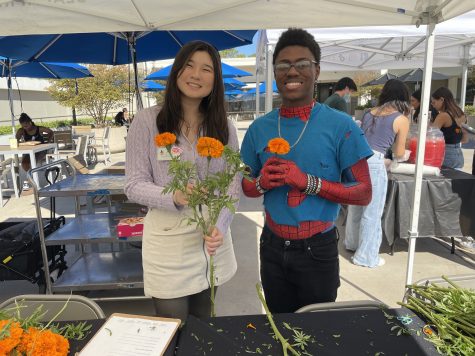 10/31/23 - USU Southwest Terrace, CSULB (from left to right): Felicity Dao and Anthony Lewis, who were working the event with 22 West Media, handed out marigold flowers to attendees who wanted to help decorate the altar.