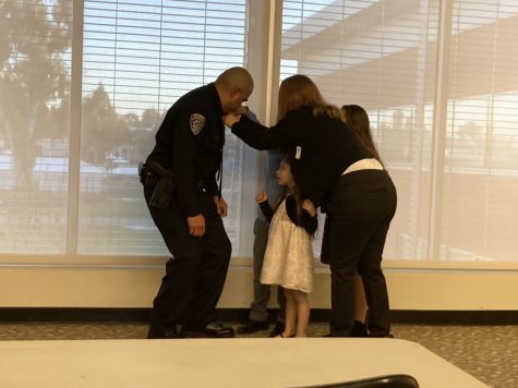 Officer Vazquez's wife Malorie Vazquez and kids help place his new badge on his uniform.